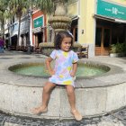 Curly-haired girl in striped dress plays with colorful balls on vibrant street