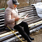 Elderly man in pink jacket reads newspaper on snowy park bench