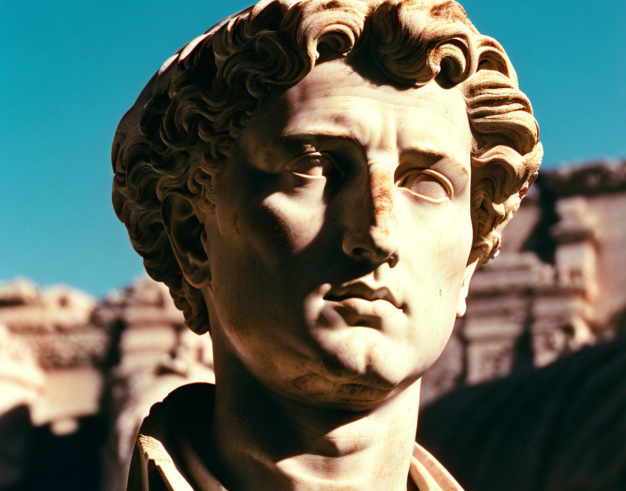 Classical statue head with intricate curly hair against ancient ruins and blue sky