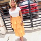 Smiling woman in white blouse and yellow skirt by colorful gate