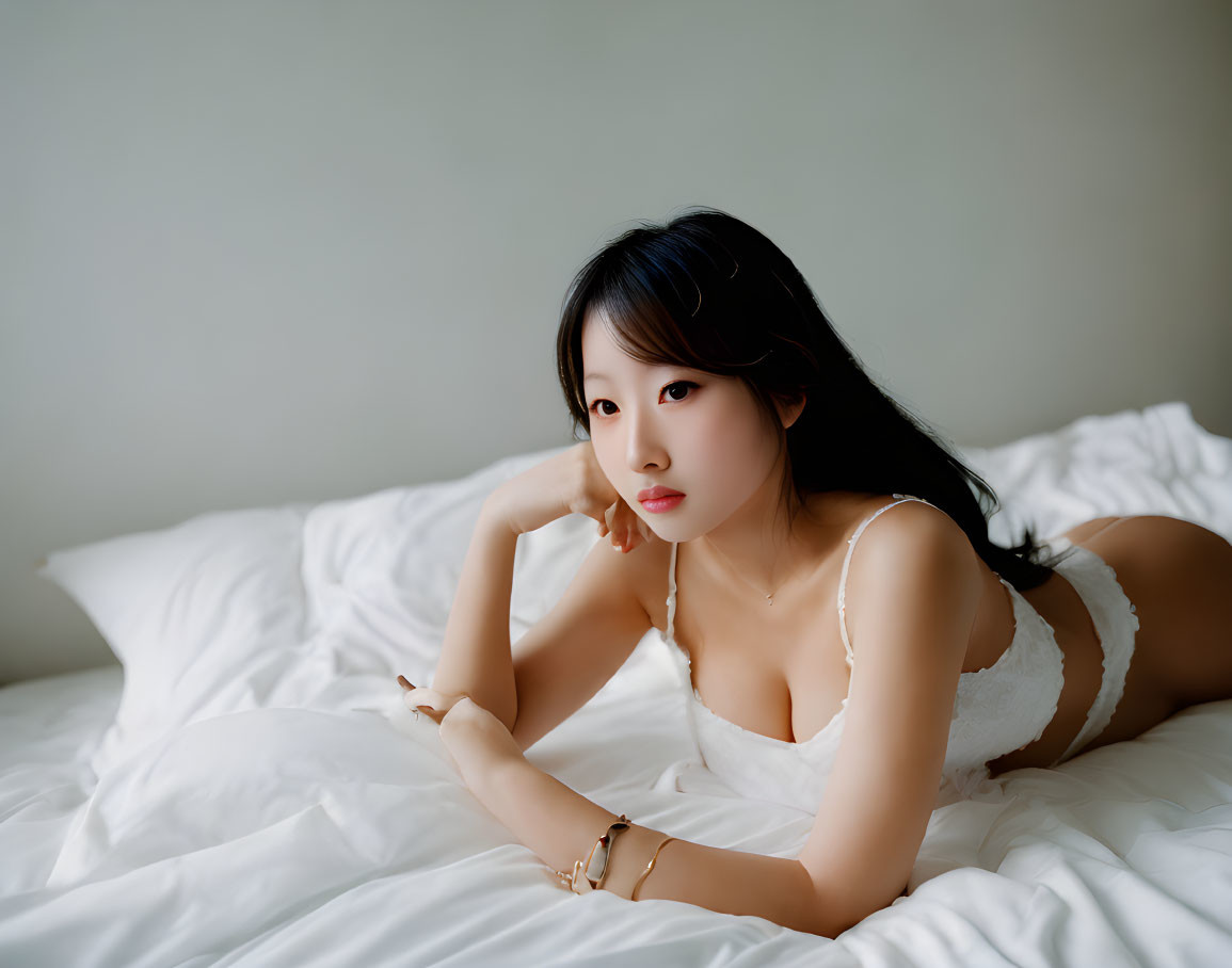 Young woman in white outfit reclining on bed with thoughtful expression