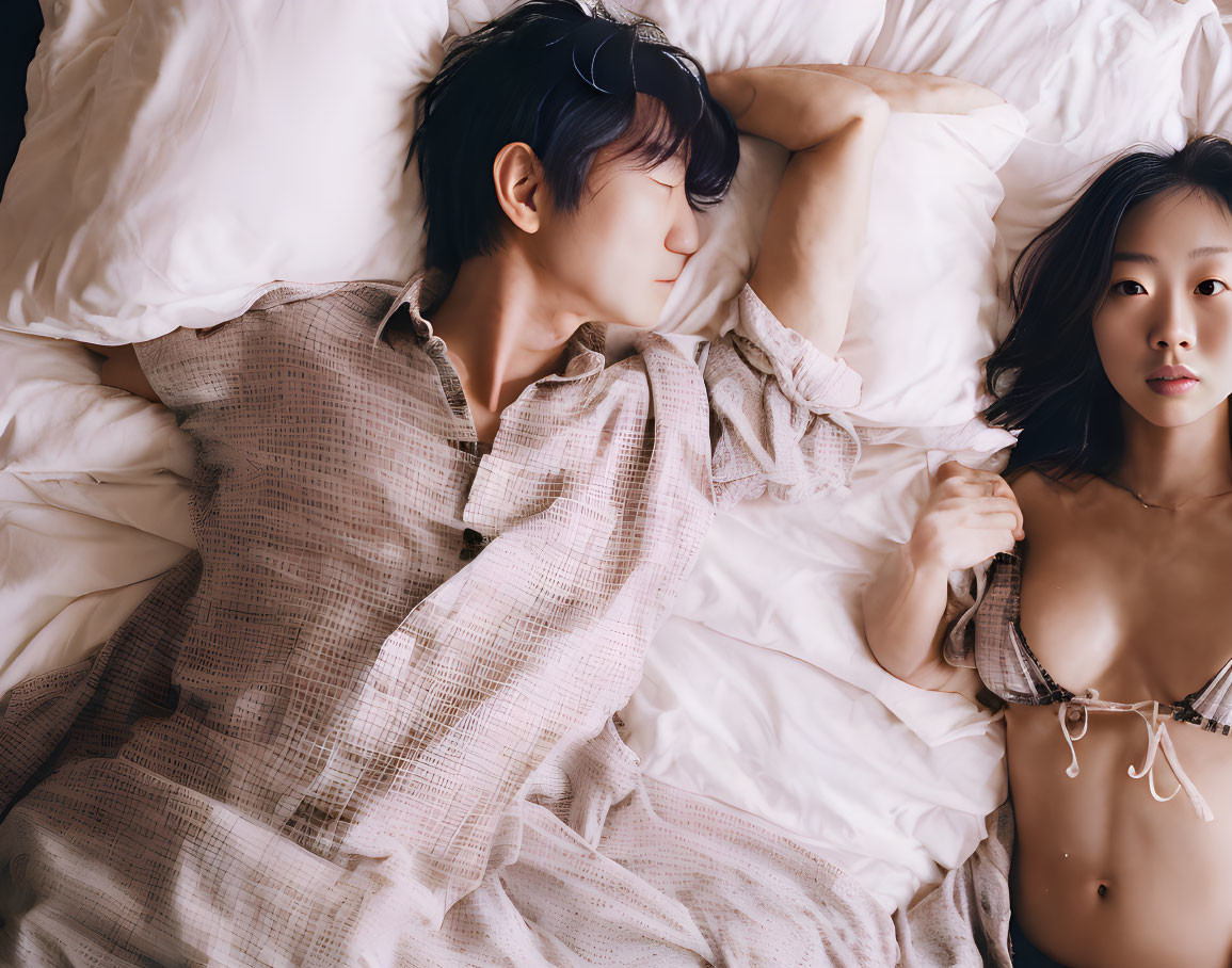 Man and woman in bed: man asleep, woman looking at camera neutral.