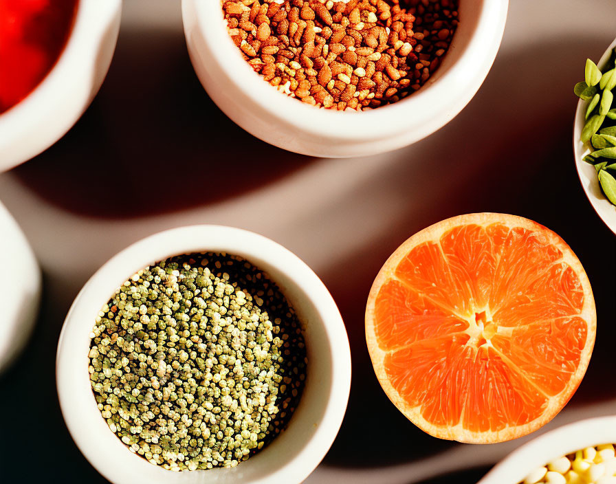 Colorful spices and half-cut orange in white bowls on a warm table