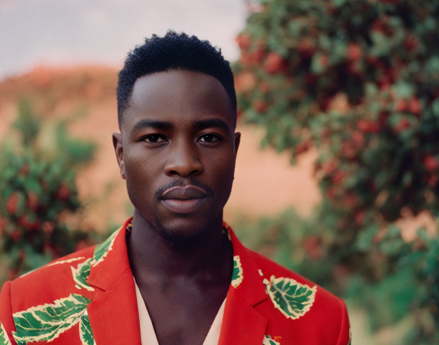 Confident man in red floral shirt with neat haircut in greenery.