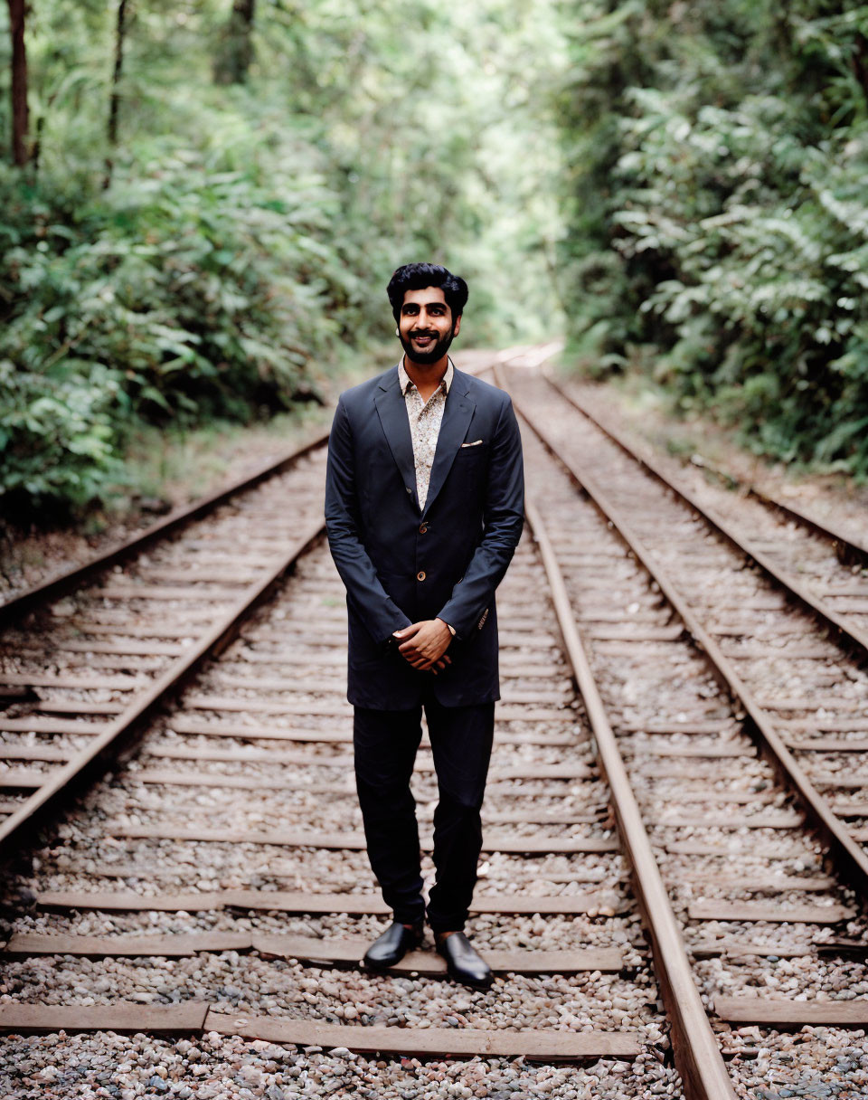 Smiling man in dark suit on forest railway track