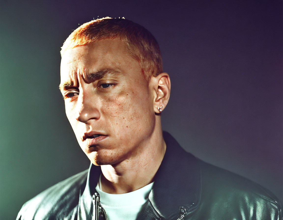 Serious man with dyed blonde hair in leather jacket on dark background