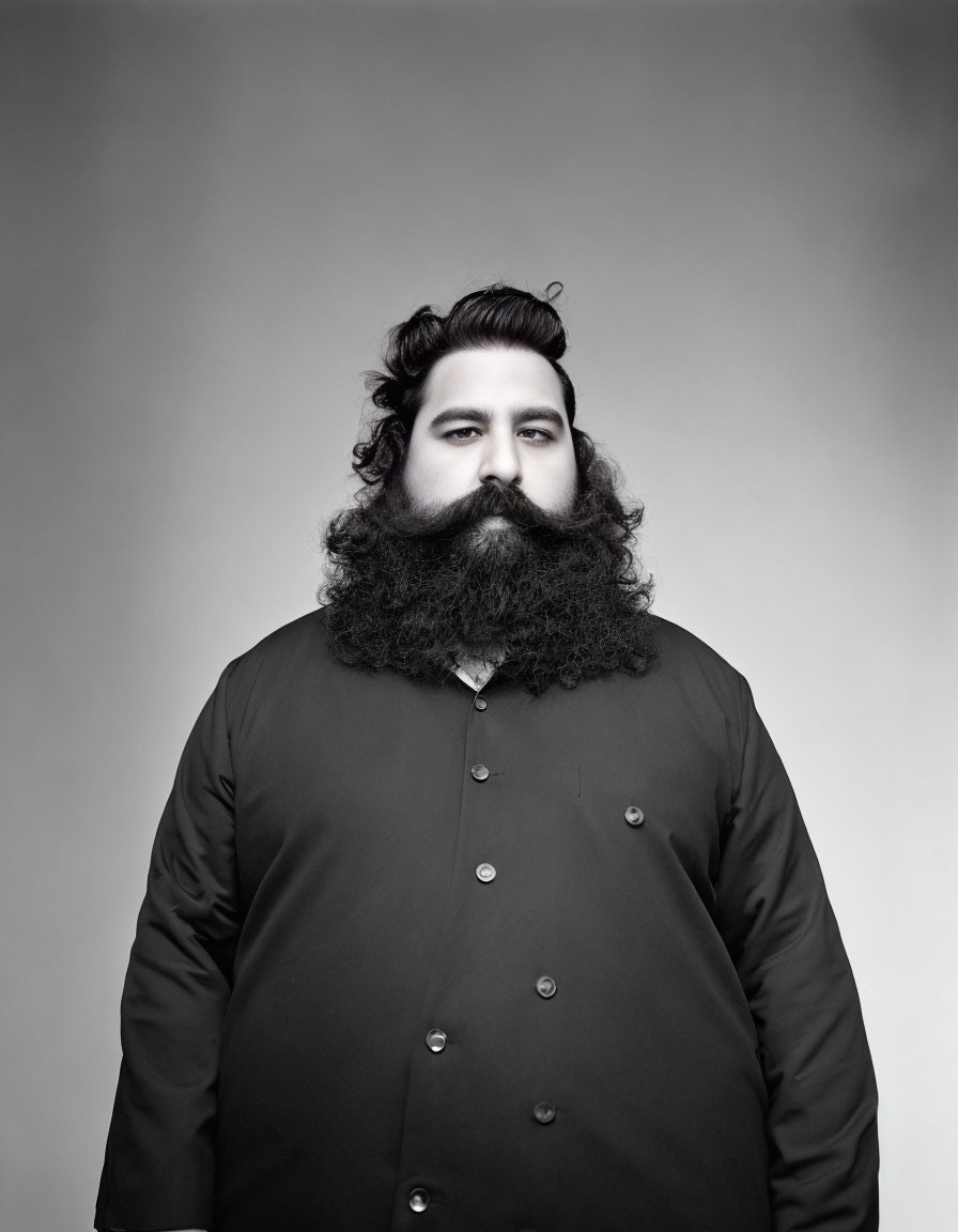 Bearded man in double-breasted coat against gray backdrop