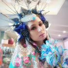 Purple-haired woman with floral crown surrounded by flowers and butterflies in dreamy setting