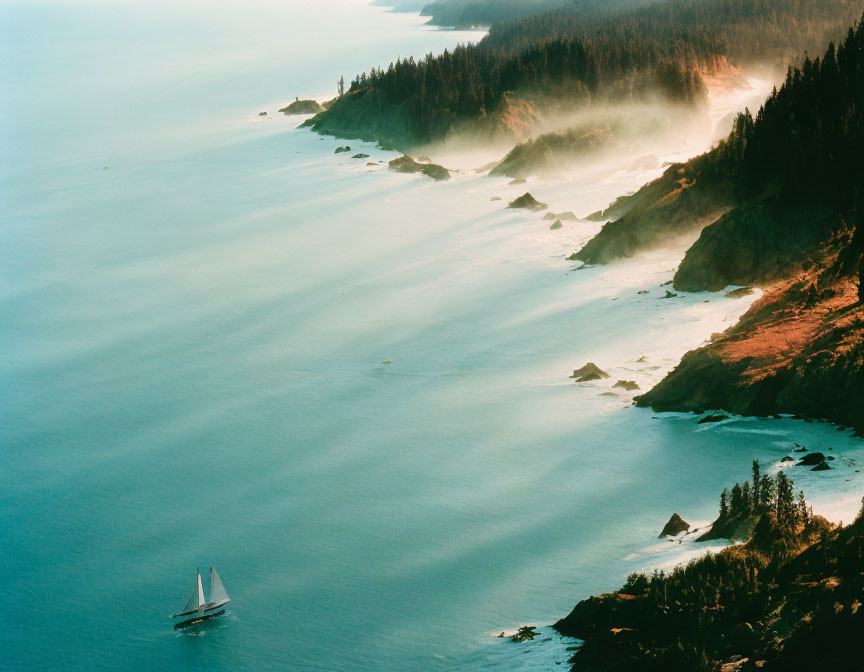 Sailboat on serene coastline with misty cliffs under warm light