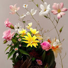 Colorful artificial flower arrangement in dark vase on neutral backdrop