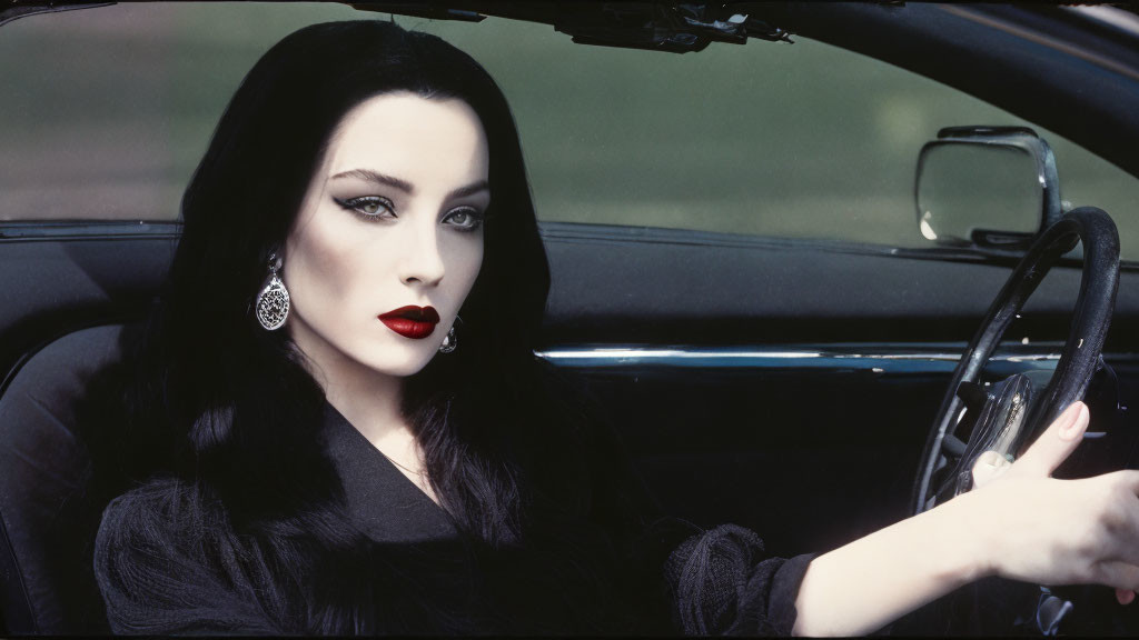 Pale-skinned person with dark hair and red lipstick in black attire behind car wheel