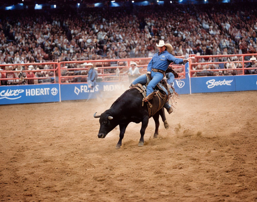 Cowboy riding bucking bull in rodeo arena with spectators.