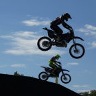 Motocross riders jumping over hill with surreal sky and birds.