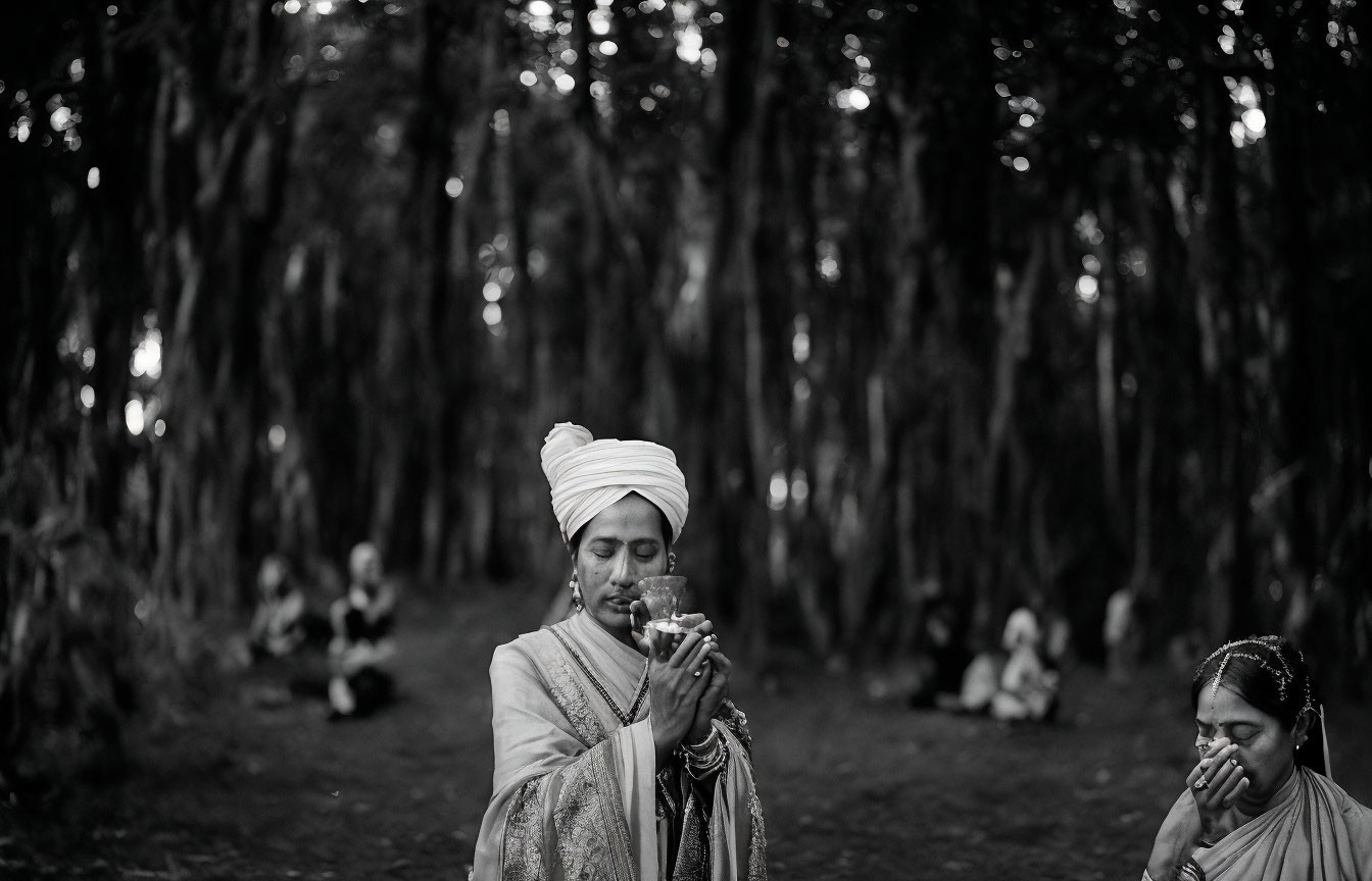 Traditional attire person praying in forest with another figure sitting