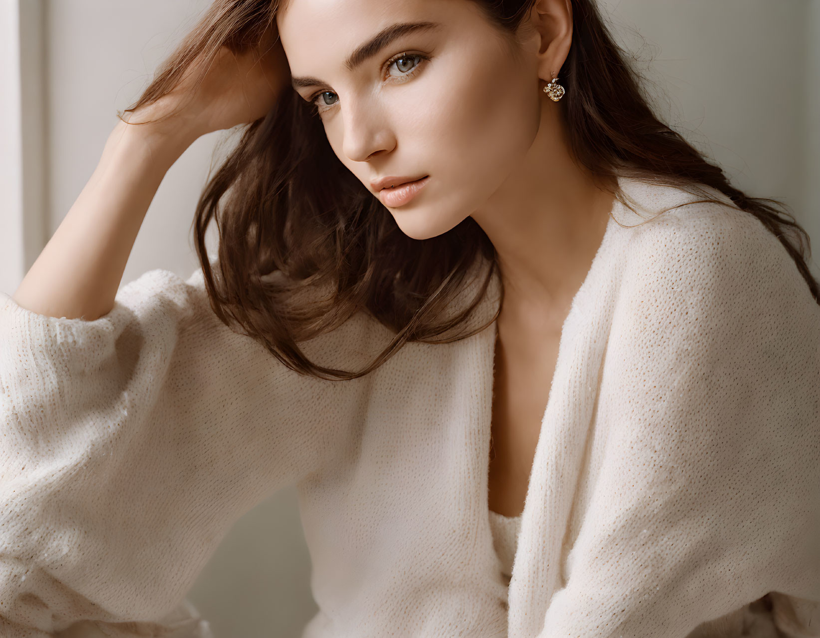 Brown-haired woman in white cardigan by window, wearing earring