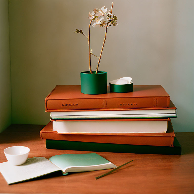 Books with leather covers, open notebook, vase with flowering branch, white bowl on wooden table