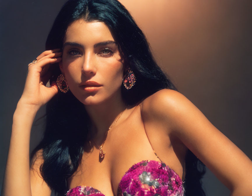 Dark-haired woman in pink dress with ornate earrings poses against soft-focus background