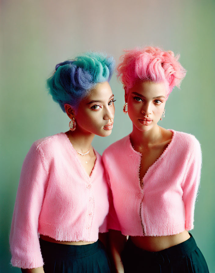 Two individuals with blue and pink hair in matching outfits pose together.