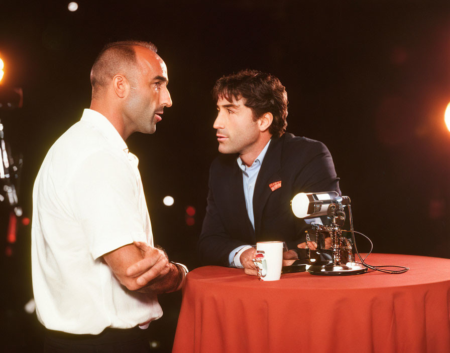 Two men in smart casual attire having a conversation with lamp and mug on table