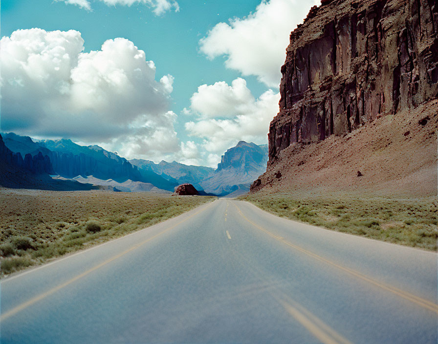 Straight Road Leading to Towering Rock Formations Under Blue Sky