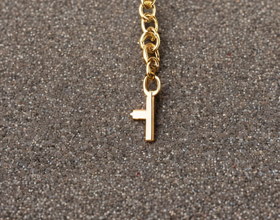 Gold chain with "F" pendant on grey textured surface