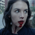 Portrait of woman with blue eyes, red lipstick, and dark hair against natural backdrop