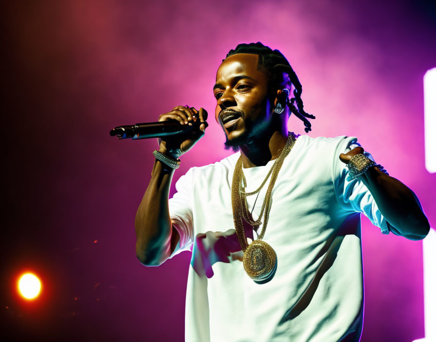 Male performer in gold jewelry under purple and yellow stage lights