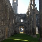 Green meadow with stone arches, towering structures, and rock formations under a sunlit sky.