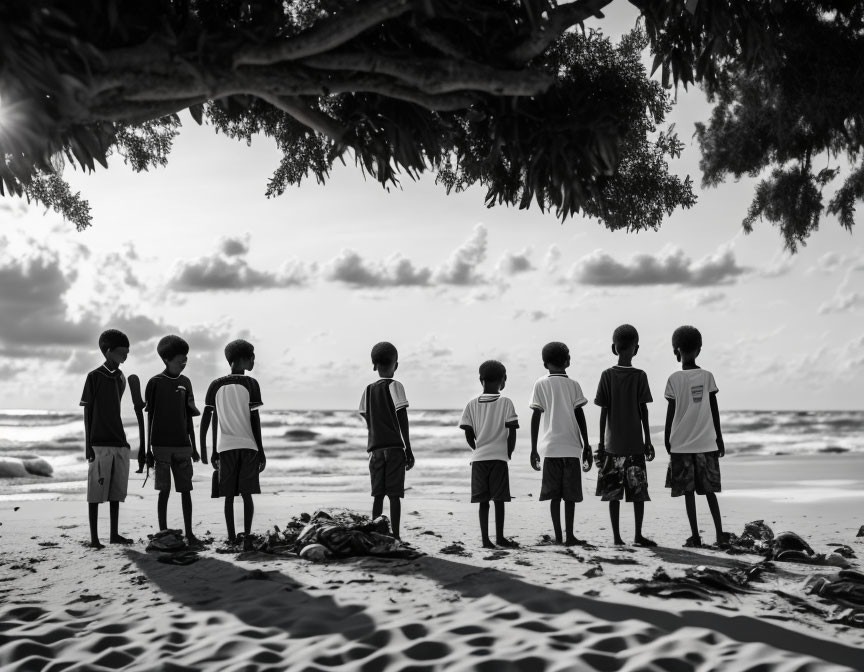 Seven children under tree at serene beach in monochrome.