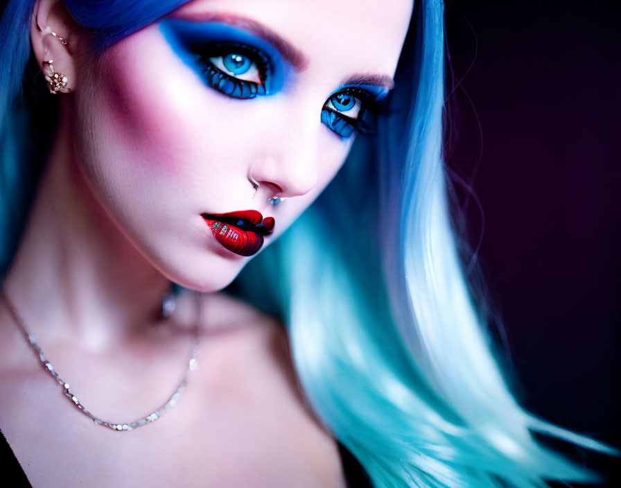 Portrait of person with blue eye makeup, nose piercing, ombré hair, holding red capsule.