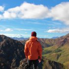 Traveler with Hat and Backpack in Front of Majestic Mountain Range