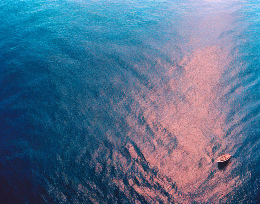 Boat floating on vast ocean with gradient water from deep blue to red