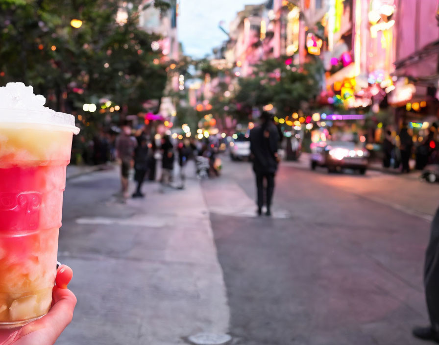 Colorful layered drink held in hand with urban street scene in background