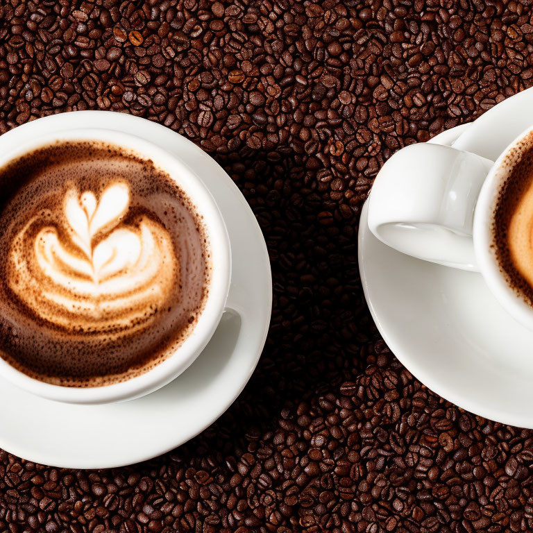 Latte art on two coffee cups with roasted beans on dark background