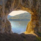 Sailing ship in sunlit cove with rocky cliffs and mountains