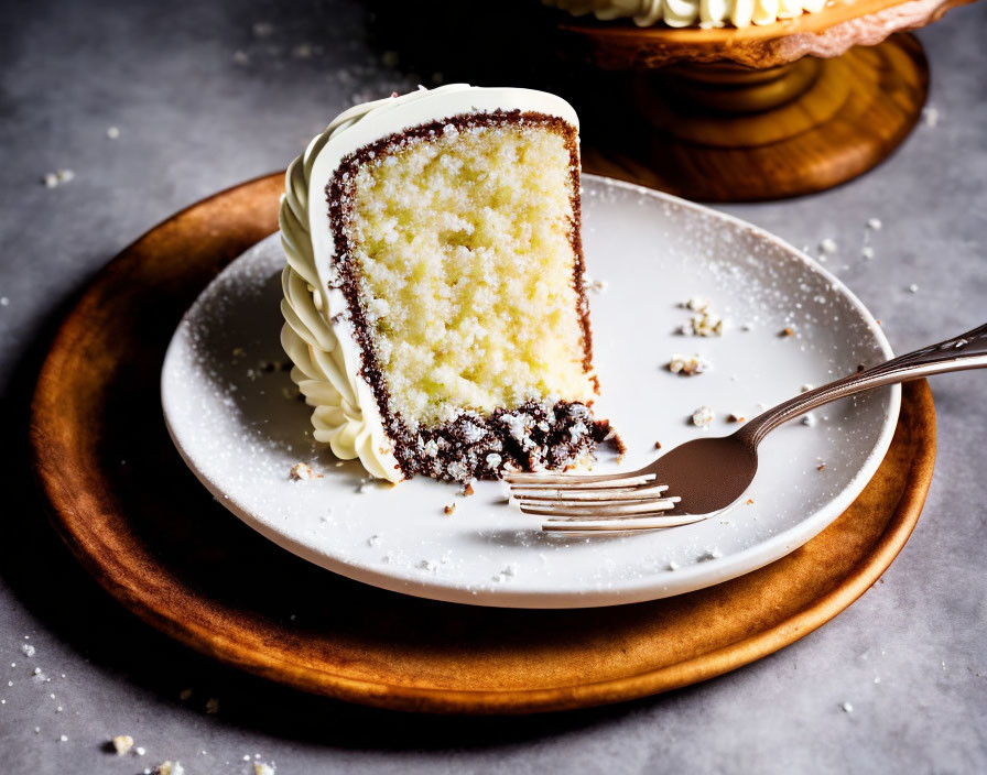 Frosted cake slice with a bite, fork, and crumbs on plate