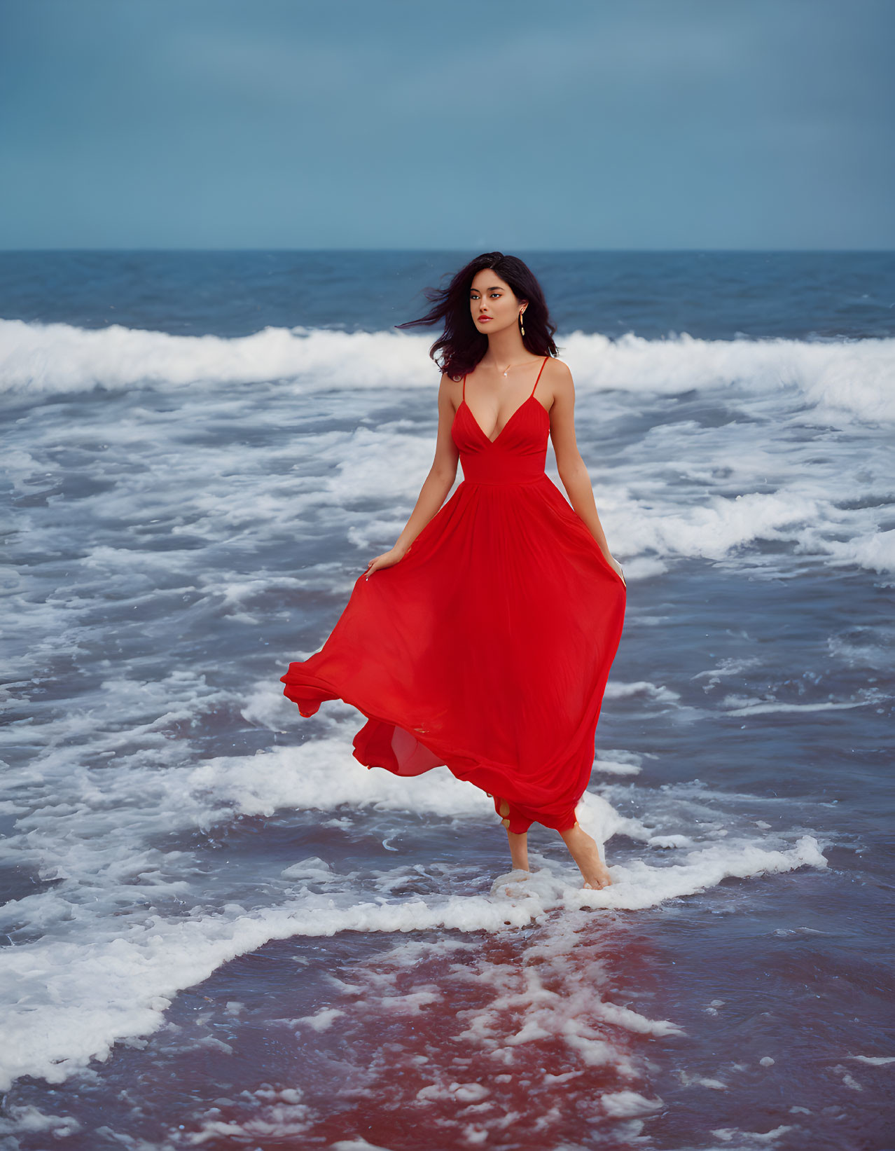 Woman in Red Dress Standing Barefoot on Beach with Waves and Cloudy Sky