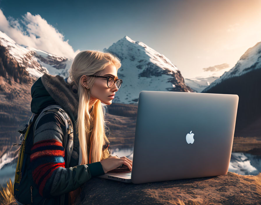 Woman with glasses working on laptop outdoors with snowy mountains and sunset sky