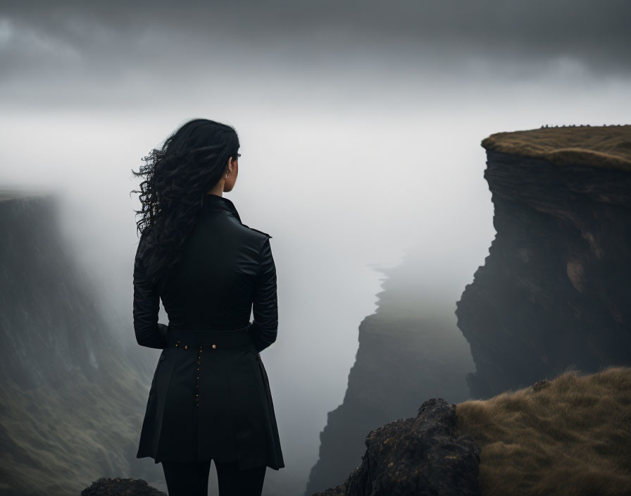 Woman in Black Jacket Gazes at Mist-Filled Valley on Cliff