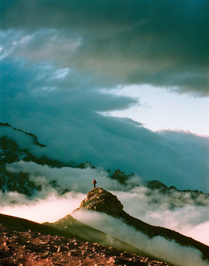 Person on rocky mountain peak above clouds at dramatic sunset