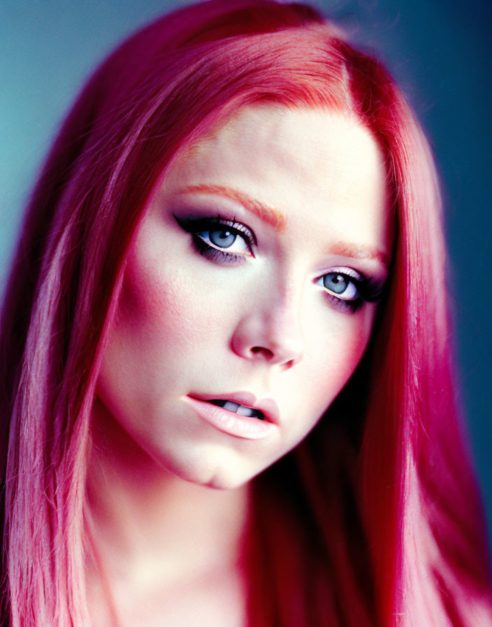 Portrait of person with bright pink hair, fair skin, dramatic eye makeup, against blue background.