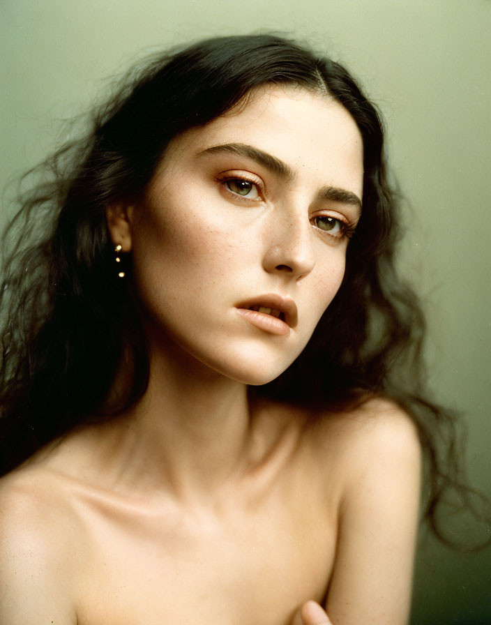 Portrait of woman with dark wavy hair and fair skin, looking pensive against neutral backdrop