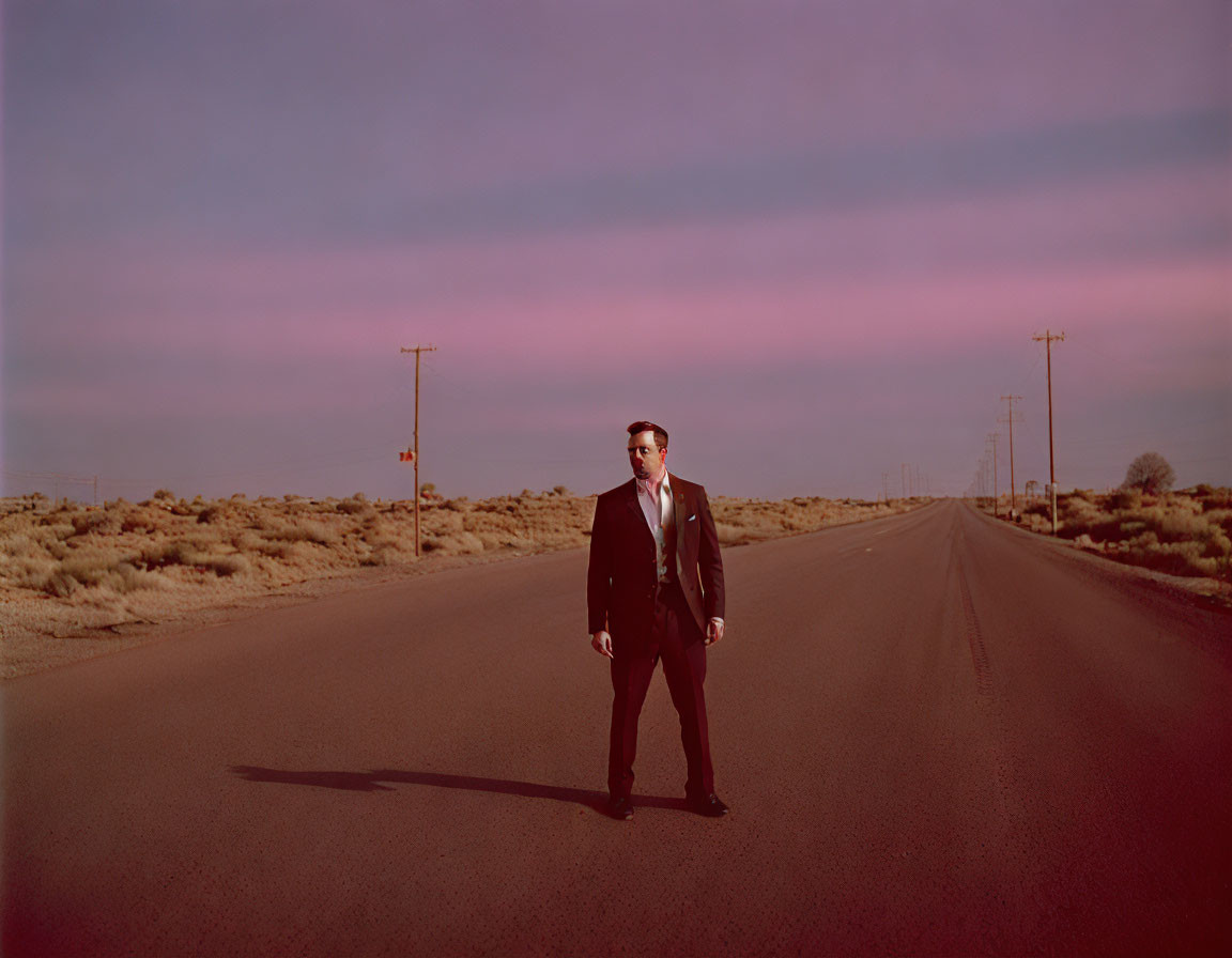 Man in suit on desert road with phone lines under dusky sky