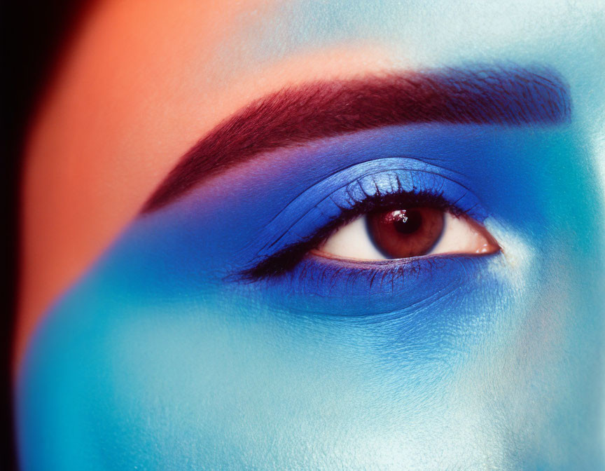 Close-up of eye with bold blue makeup and matching face paint under vibrant lighting