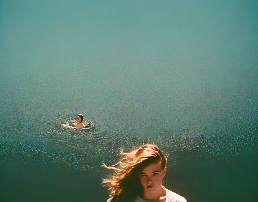 Tranquil blue water scene with floating person and windswept hair figure