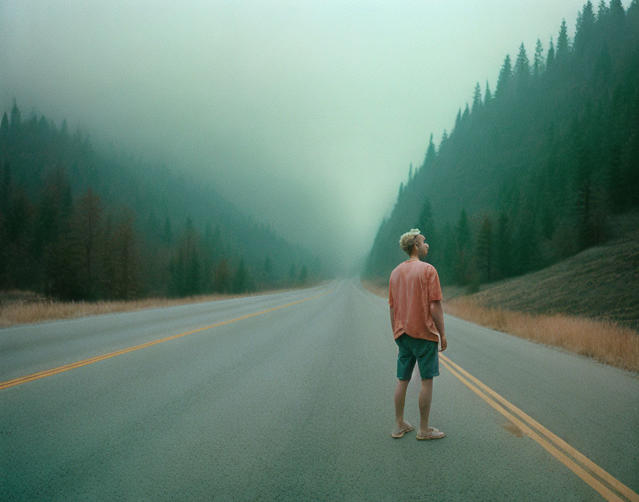 Person standing barefoot on misty road surrounded by dense forests