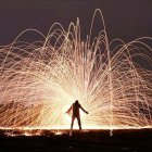 Silhouette of person in mystical night scene with bare trees, fireflies, glowing particles, and moon