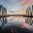 Surreal landscape with tall arch structures, multiple moons, pink clouds, and reflections on tranquil water