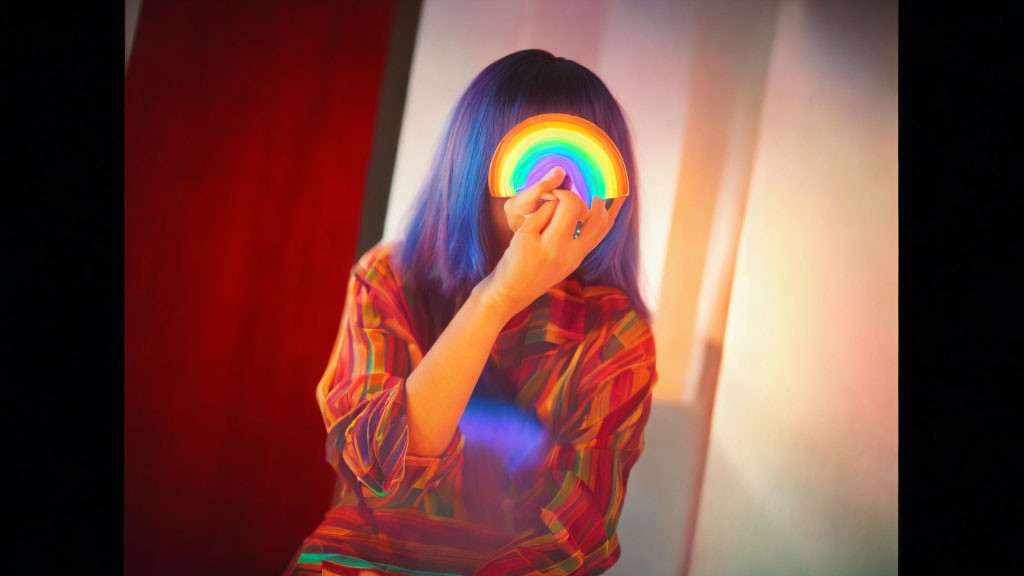 Blue-haired person with rainbow disc and colorful shirt against red curtains