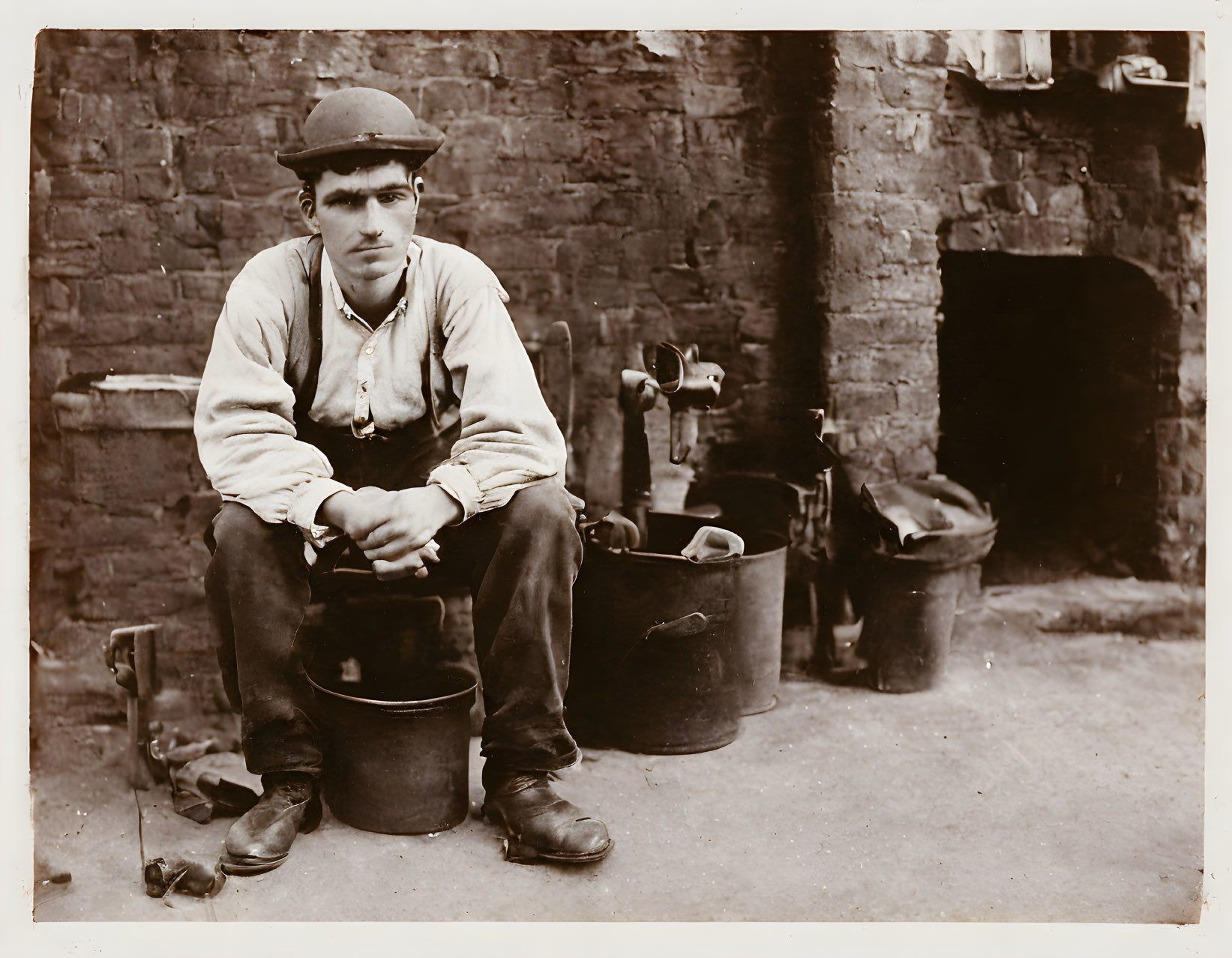 Vintage work attire young man on bucket with brick wall and shoe-shining equipment.